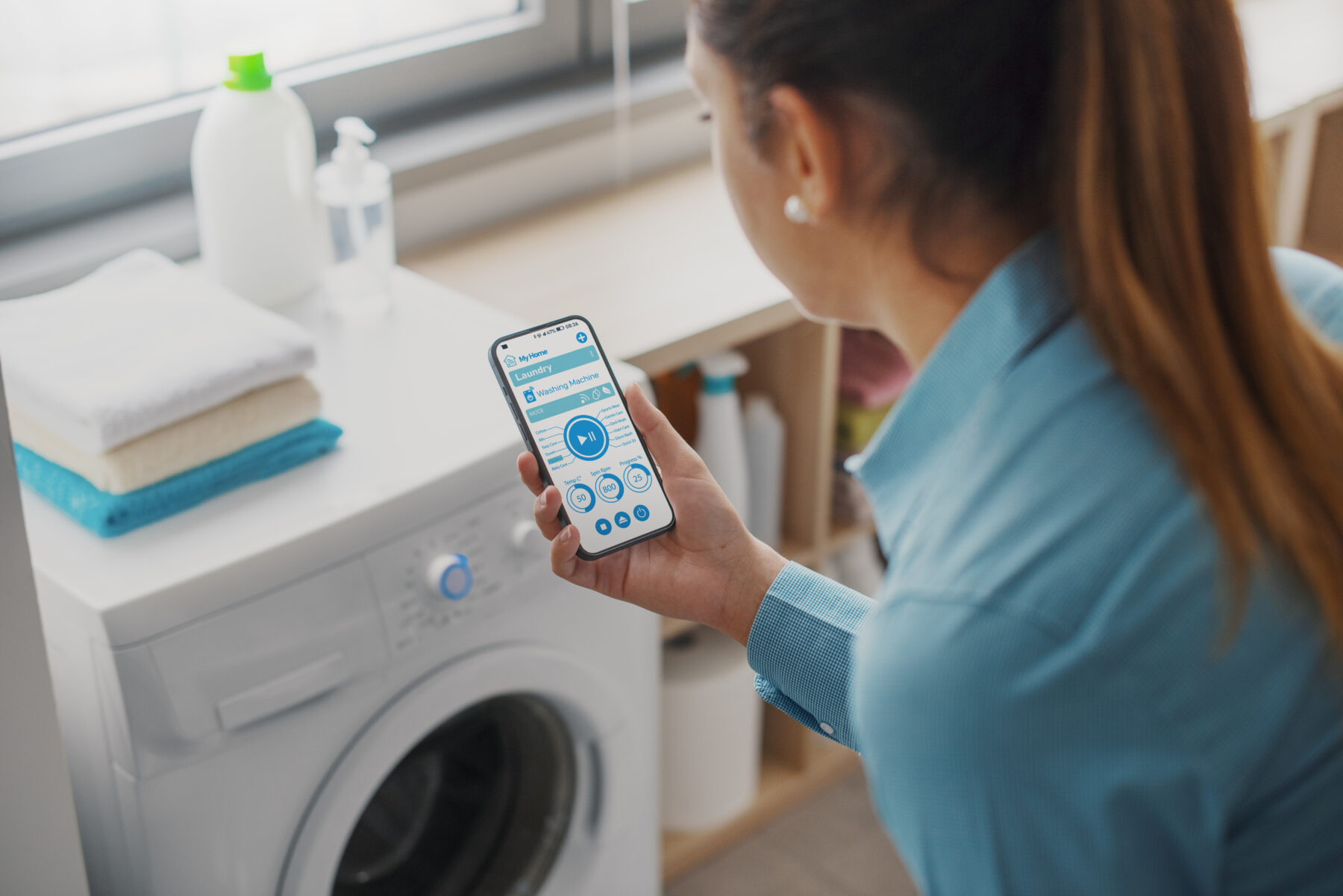 CleanTech Innovation - Woman using a smart washing machine, she is controlling the appliance from her smartphone